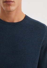 Donkerblauwe ribgebreide trui van een textiele stof met een klassieke ronde halslijn, met een aansluitende pasvorm rond de hals en schouders.