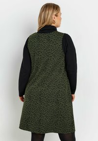 Vihreä leopardikuosiset mekko, jossa on istuva malli ja A-linjainen muoto. Sisältää mustan pitkähihaisen paidan kerroksittain. 