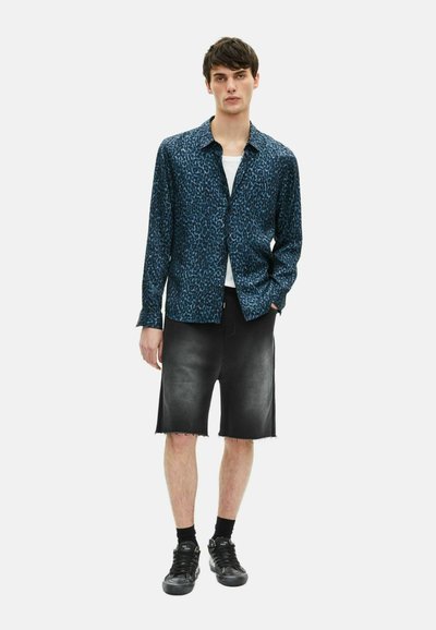 Korteblauwe leeuwenprintshirt met korte mouwen, gecombineerd met zwarte denimshorts met een ruwe zoom, gedragen met zwarte sneakers en zwarte sokken.