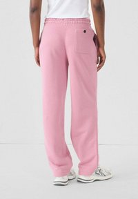 Roze sweatpants met een relaxte pasvorm, elastische tailleband en een enkele achterzak. Draagt met een wit shirt en sportieve schoenen.