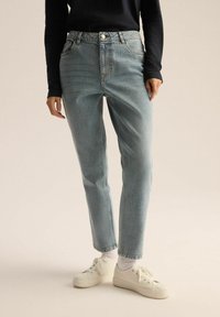 Jasnoniebieskie dżinsy z wysokim stanem i prostymi nogawkami. W zestawie z białymi sneakersami i dopasowaną czarną bluzką z długim rękawem.