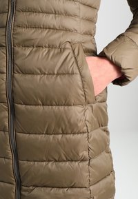 Chaqueta de plumas color caqui con acolchado horizontal, que presenta un cierre frontal y bolsillos laterales. Tela suave y brillante con una textura ligeramente acolchada.