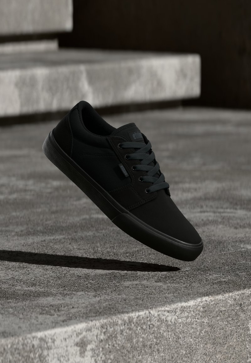 Tenis de culoare neagră cu o finisare netedă, mată. Dispune de un design cu șnur, laturi texturate și o talpă din cauciuc flexibilă, cu un model.