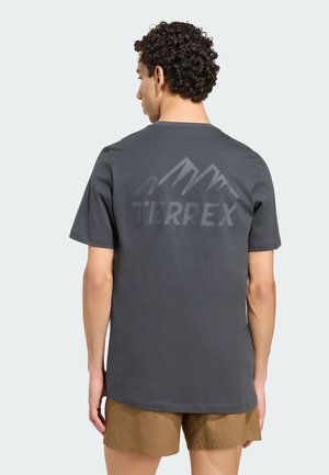 Mand med krøllet hår iført en mørkegrå TERREX t-shirt med bjerglogo og lysebrune shorts, vendt væk fra kameraet.