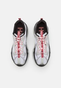 Un paio di scarpe da ginnastica bianche e grigie con lacci rossi e bianchi, fodera interna nera e linguette rosse viste dall'alto su sfondo bianco.