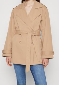 Beige trenchcoat met een dubbelzijdig ontwerp, brede revers, een ceintuur in de taille en knoopmanchetten. Glad, lichtgewicht stof.