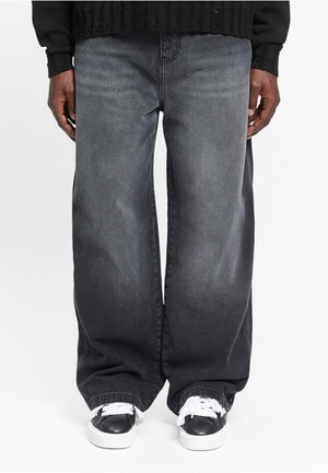 Wide-leg black denim jeans featuring a faded finish and slight texture, paired with black and white sneakers.