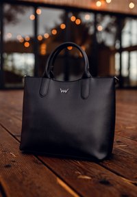 Black leather tote bag with a smooth texture, featuring short handles and a subtle logo accent. Sturdy rectangular shape.