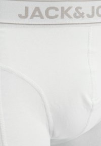 Białe bawełniane slipy z szarym elastycznym pasem w talii, na którym widnieje nadruk "JACK & JONES" dużymi literami. Gładka faktura, dopasowany krój.