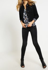 Zwarte spijkerjacket met twee voorzakken, gecombineerd met een geblokt topje in tinten blauw, en zwarte skinny jeans aangevuld met enkellaarsjes.