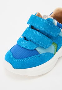 Kék sportcipő, amely kék velúr és hálós anyagok kombinációjával készült, két állítható tépőzárral és fehér gumitalppal.