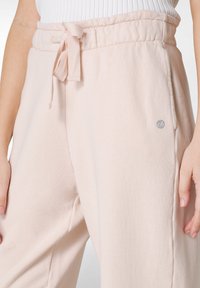 Rosa sweatpants gjorda av mjukt material med elastisk midja och dragsko samt en liten logodetalj på vänster sida.
