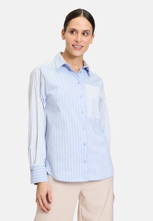 Camicia a righe blu chiaro e bianco con bottone, una tasca sul petto, maniche lunghe e orlo curvo. Realizzata in tessuto traspirante.