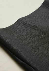 Black fabric with a textured pattern featuring small circular motifs. The material appears soft and flexible with a smooth surface.