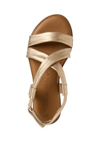 Gold metallic sandal featuring crisscross straps, a soft brown insole, and an adjustable ankle strap with a side buckle. Flat sole design.
