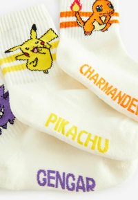 Weiße Knöchelsocken mit Pikachu-, Charmander- und Gengar-Designs, verziert mit bunten Streifenakzenten und gestickten Charakternamen.