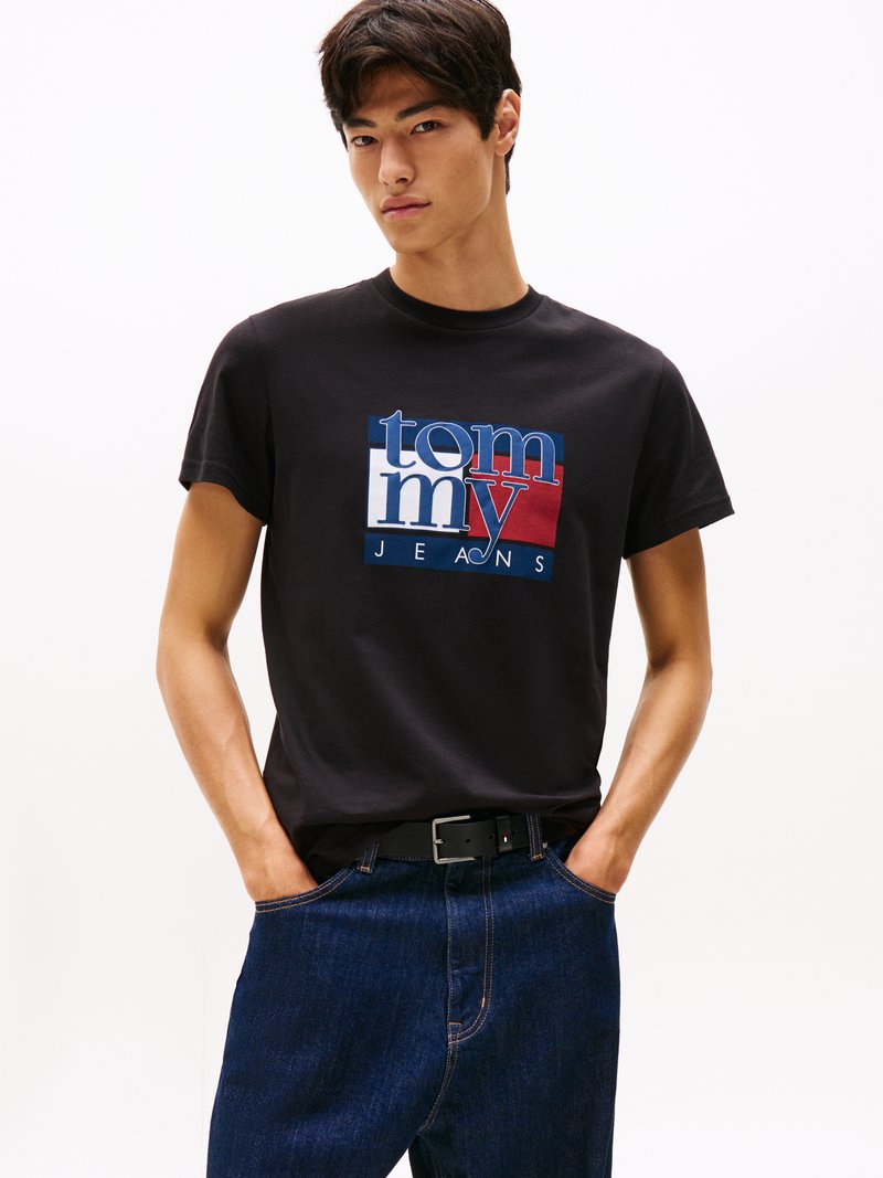 Melna kokvilnas t-krekls ar stilizētu "Tommy Jeans" logo zilos, sarkanos un baltos toņos. Valkāts ar tumši ziliem džinsiem un melnu jostu.