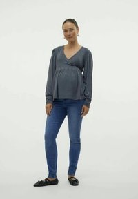 Siva dolga majica z obwrapanim pasom, kombinirana z modrimi ozkimi jeansom in črnimi ravnimi čevlji. Preprost, mehak material in čist dizajn.