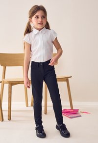 Valkoinen lyhythihainen nappipaita, jossa on koristeommeltu sisustus, yhdistettynä mustiin slim-fit-housuihin ja kiiltäviin mustiin kenkiin.