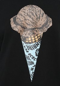 Zwarte shirt met een afbeelding van een gestructureerde ijsschep bovenop een lichtblauwe hoorntje, met verschillende zwarte teksten en patroon details.