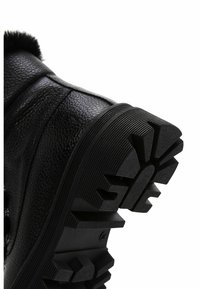 Bota negra texturizada con suela de goma que presenta profundas ranuras y un diseño grueso y resistente para mayor tracción. Acentuada con un suave borde de piel de pelo en la parte superior.