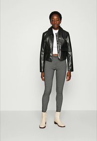 Sort cropped jakke i kunstlær med to frontlommer, hvit cropped topp, grå mønstrete leggings og offwhite ankelstøvler.