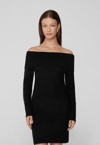 Černé pletené šaty bez ramínek s dlouhými rukávy, jemně strukturované, přiléhavého střihu a s délkou ke středu stehna.