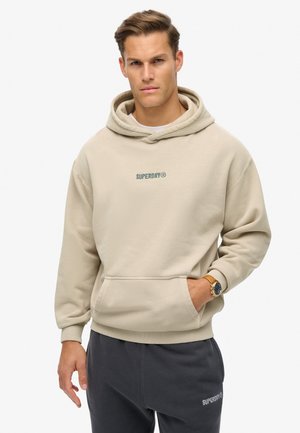 Beige hooded sweatshirt with front pocket, featuring embroidered green "SUPERDRY" logo. Soft texture, relaxed fit, ribbed cuffs.