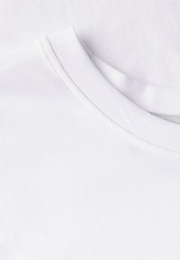 Bílý bavlněný tričko s kulatým výstřihem, hladkou texturou a jemně šitými švy. Tkanina se zdá být lehká a prodyšná.