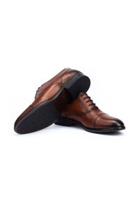 Scarpe eleganti in pelle marrone con finitura liscia, design con lacci, punta arrotondata e suola in gomma nera testurizzata con un motivo geometrico.