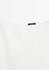 Vêtement blanc avec des coutures verticales et une petite étiquette noire portant la mention « Massimo Dutti Made in China » à l'arrière du col.