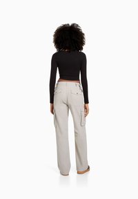 Černý dlouhý rukáv crop top v kombinaci se světle šedými cargo kalhotami s bočními kapsami a volným střihem, pohled zezadu.
