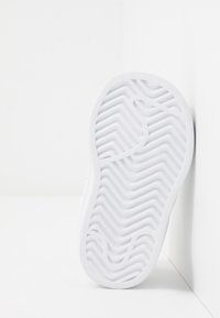 Vitt sneakersula med ett texturerat zigzagmönster, platt design och formgjord gummimaterial. Enkel och slank profil mot en ljus bakgrund.