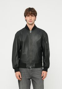 Melna ādas bomber jaka ar priekšējo rāvējslēdzēju, ribotām aprocēm un sānu kabatu ar rāvējslēdzēja aizdari. Gluda tekstūra, klasiskā dizains.