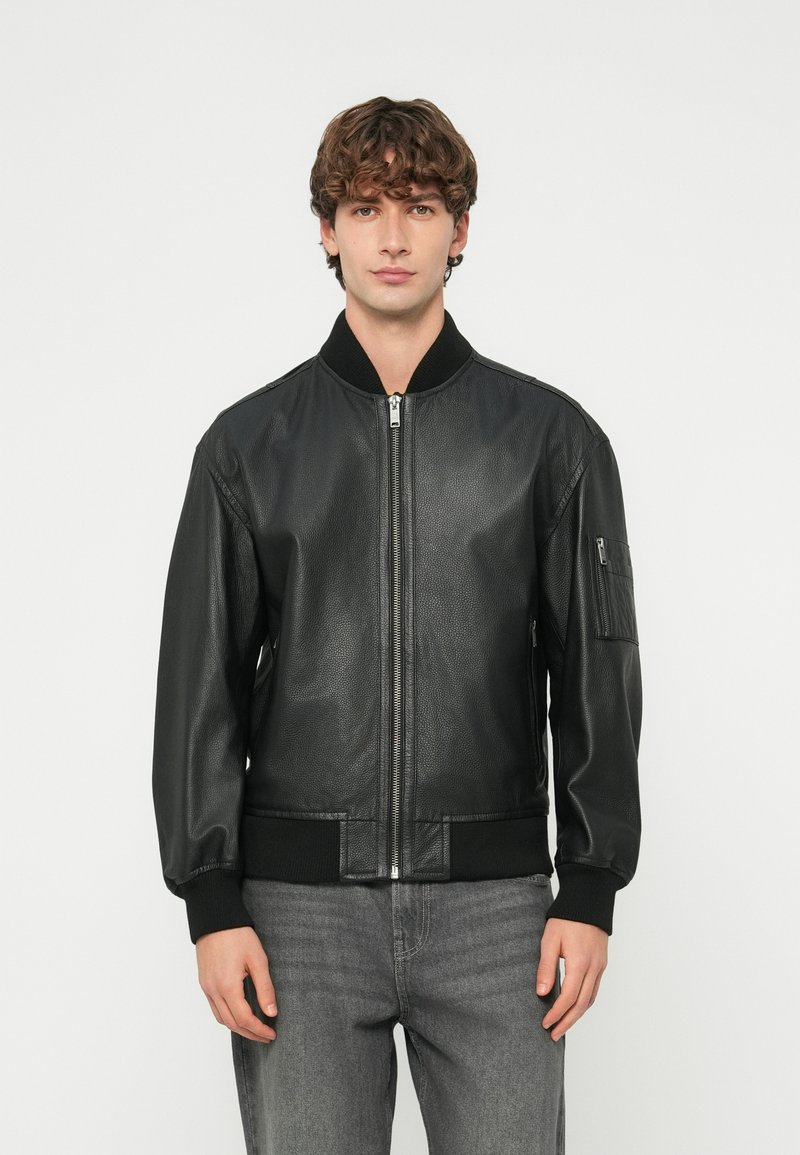 Melna ādas bomber jaka ar priekšējo rāvējslēdzēju, ribotām aprocēm un sānu kabatu ar rāvējslēdzēja aizdari. Gluda tekstūra, klasiskā dizains.