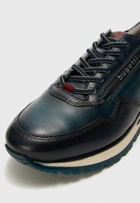 Navy Leder-Sneaker mit strukturierten Oberflächen, verziert mit dekorativen Nähten, blauen Schnürsenkeln, rotem Akzentband und einer Gummisohle mit Profil.