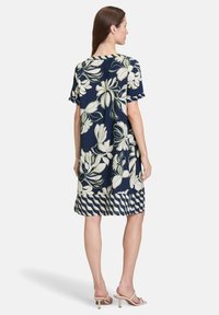 Námořnická modrá květinová šaty s krátkými rukávy, zdobená velkými bílými květinovými vzory a pruhovaným lemem. Vyrobeno z lehkého materiálu.