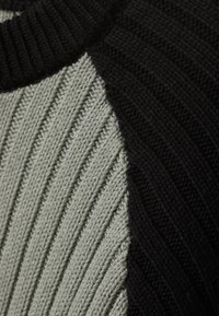 Knit pullover featuring a ribbed texture. Grey and black color blocks intersect at the shoulders, with a rounded neck and smooth finish.