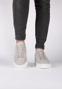 Sneakers in suede grigio chiaro con suole in gomma bianca, punta rotonda e lacci piatti. Jeans skinny neri parzialmente visibili.