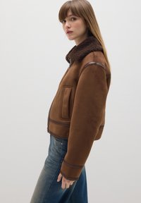 Bruine bomberjack van suede met een textuur, een donkerbruine bontkraag, voorzien van een voorzak en leren accenten op de manchetten.