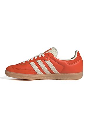 Zapatilla naranja de perfil bajo con cordones blancos, tres franjas laterales blancas texturizadas, lengüeta beige y suela de goma sobre fondo blanco.