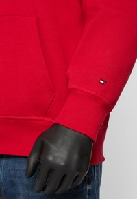 Felpa rossa con cappuccio, dotata di tasca frontale e polsini a costine. Presenta un piccolo logo del marchio in blu navy, bianco e rosso sulla manica. Tessuto in misto cotone.