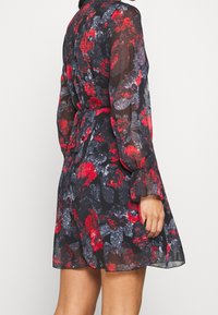 Vestido negro con estampado floral en rojo y gris, de mangas largas y transparentes, cintura con lazo y dobladillo acampanado, adecuado para uso casual.