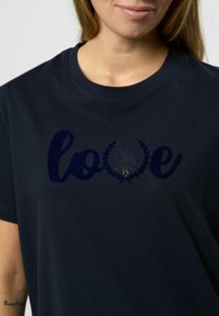 Temno modra bombažna majica z wordom "ljubezen" v temno modri barvi in dizajnom lovorjevih listov, gladka tekstura in krožni izrez.