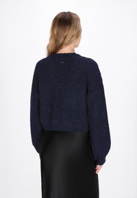 Maglione corto a maglia in blu navy con texture a coste e maniche lunghe, caratterizzato da un leggero luccichio. La vista posteriore mostra un collo rotondo.