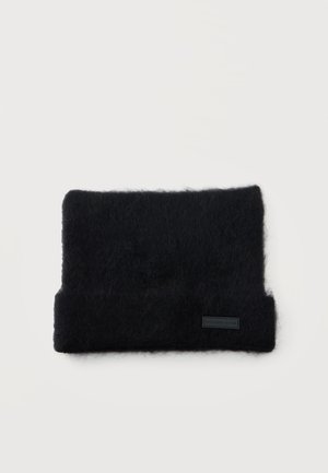 Pochette rectangulaire en tissu noir à texture duveteuse, avec une partie inférieure repliée et une petite étiquette, sur fond blanc.