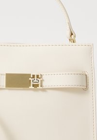Borsa a mano crema con una texture in pelle liscia, dotata di un dettaglio hardware rettangolare in tonalità oro e una tracolla stretta.