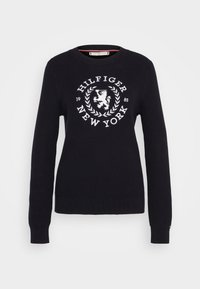 Pull en maille marine avec un col rond, des manches longues et un logo blanc brodé en évidence "HILFIGER NEW YORK" accompagné d'un motif de lion.