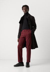 Manteau trench noir, col roulé noir ajusté, pantalon bordeaux et baskets noires. Tissu lisse, coupe ajustée, design minimaliste.