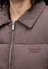 Veste matelassée marron avec une fermeture éclair en métal et un col, arborant "tommy jeans" brodé sur la poitrine gauche.